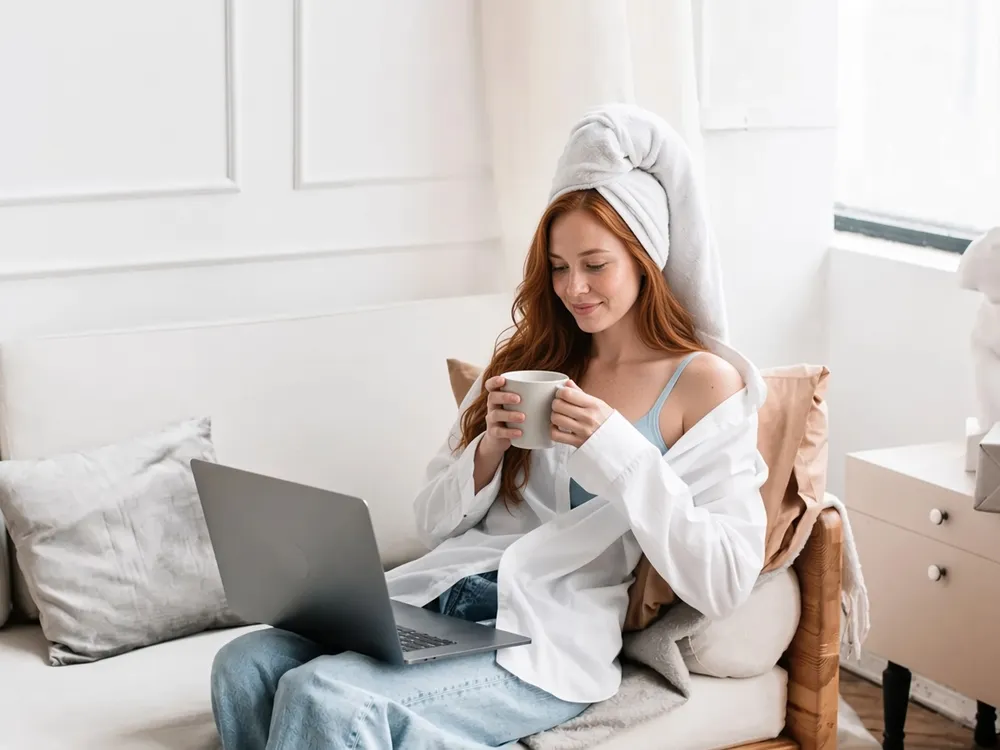 A woman relaxing on a sofa with a mug and a laptop